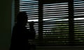 Silhouette of an unrecognisable person looking out of a window blind.