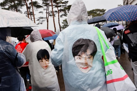 BTS fans hold umbrellas while wearing raincoats featuring the band member Jin