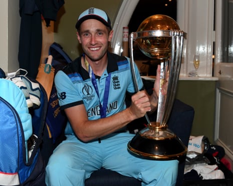 Chris Woakes holding the World Cup trophy with the winners' medal around his neck in the dressing room