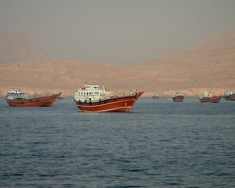 Several large wooden boats with reddish-brown hulls are anchored in calm blue water with hazy mountains behind