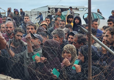 Crowds of people reach through a wire fence while awaiting supplies.