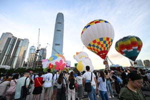 A crowd look on as hot-air balloons prepare for take off against a backdrop of the city skyline