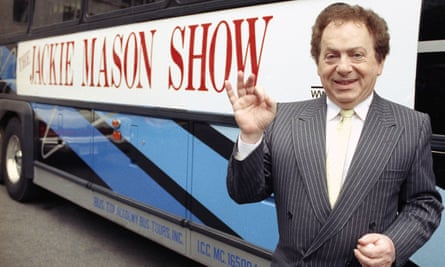 Jackie Mason standing beside a bus displaying a sign advertising his TV show in 1992.