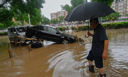 A man wades past a damaged car along a flooded street in Beijing’s Mentougou district, where cars were washed away and subway stations were inundated.