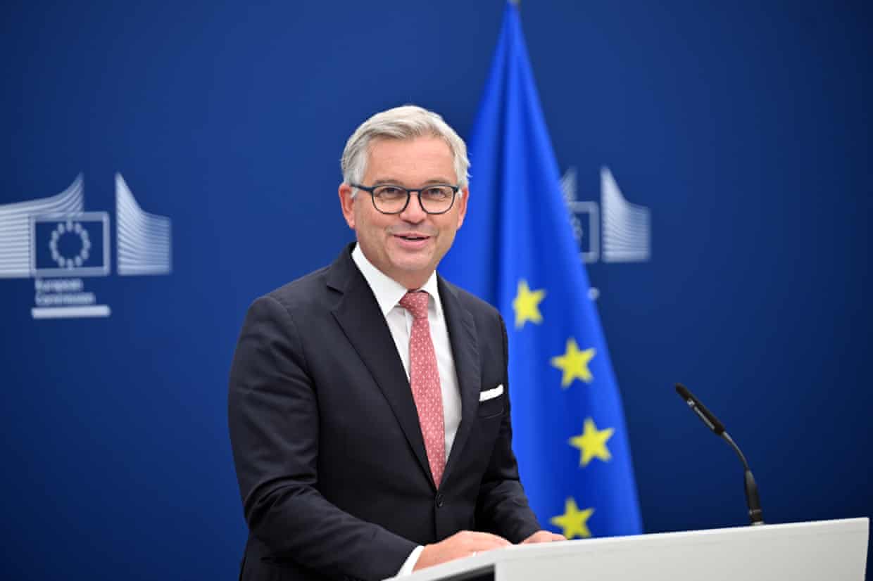 Magnus Brunner speaks during a press conference, standing in front of a furled EU flag.