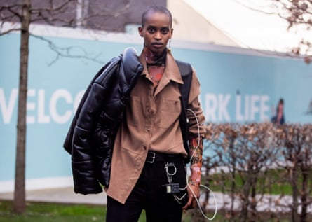 Model wears a skull earring, black vegan leather jacket, brown shirt, black pants and an old mobile phone keychain on her belt.