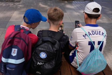 Three boys use their phones while sitting outside a school in Sydney