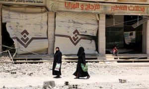 Two women walk by a building hit by an airstrike in Damascus, Syria