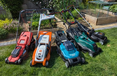 Five lawnmowers on a lawn in a green garden with planters behind them