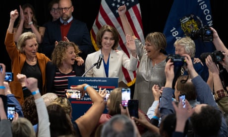 people in a crowd cheering for a woman standing at a podium