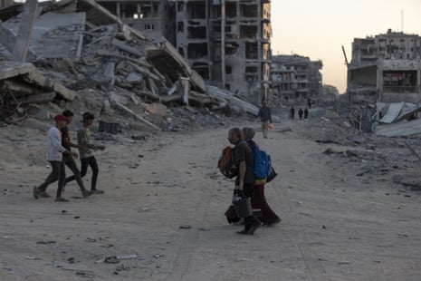 Palestinian people walk among the rubble of buildings destroyed by Israeli attacks in Gaza City.