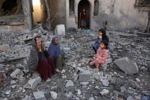 Palestinian women and children sit on blocks of rubble