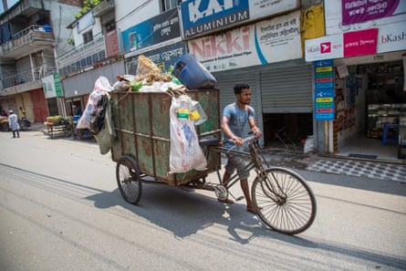 A man pushes a waste-laden rickshaw along a street