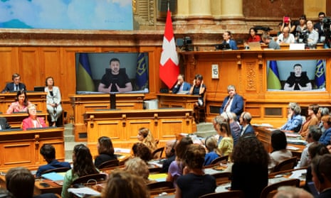 Zelenskiy, shown on screens, addresses the Swiss parliament in Bern via video link on Thursday