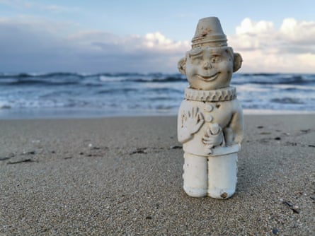An old clown-shaped bottle stands near the shore on a beach.