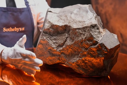 Sotheby’s worker in a blue overall and white gloves holds a large grey meteorite