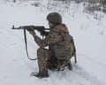 Soldier in camouflage kneels in the snow pointing a rifle