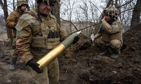 A Ukrainian soldier loads a shell into a British-made L119 howitzer, watched by two others behind
