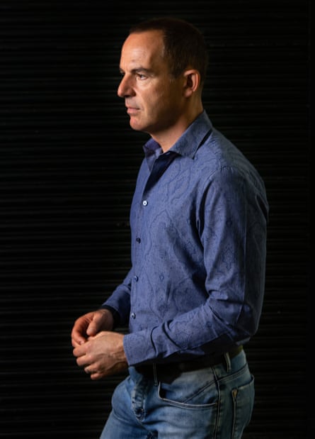 A profile of Lewis in blue shirt and jeans with a black background behind him