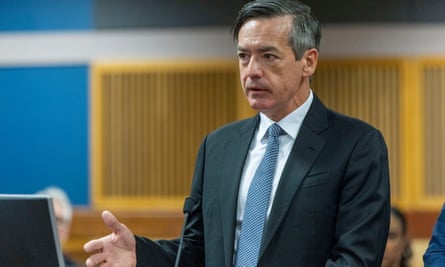 White middle-aged man in suit speaks and gestures with right hand in courtroom.