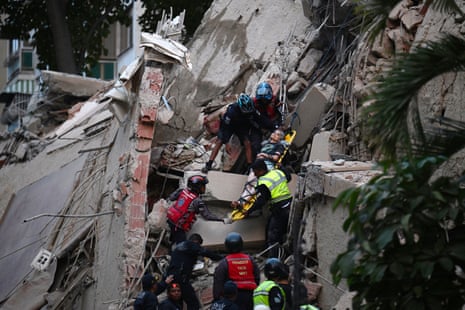 Emergency workers carry a person on a stretcher through rubble and debris of a collapsed building