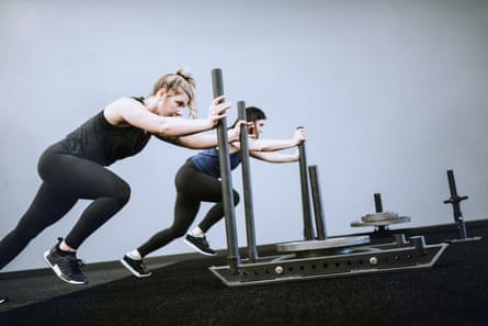 A man and woman exercising push weighted sleds with looks of determination.