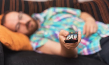 A man lying on the sofa with a remote control in his hands.