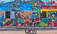 a boy rides his bike past a mural by Barbara Siebenlist decorating the side of a building on Brazil Lane in Jamestown.
