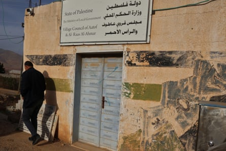 Abdullah Bsharat walks away from a closed door of a building. A sign above the door describes it as the village council and part of the state of Palestine.