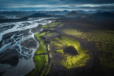 Aerial view in Iceland of braided river channels beside a mossy green volcanic crater