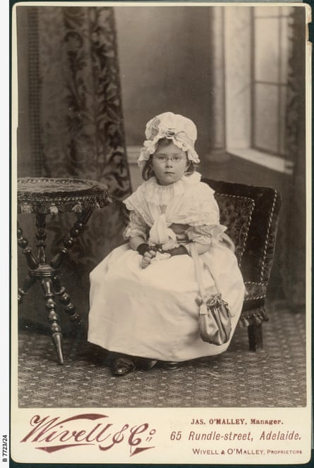 An eight-year-old girl wearing a white dress, a white lace bonnet and glasses