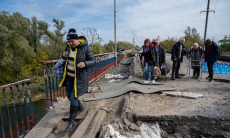 People flee west on foot across a heavily damaged bridge over the Oskil River.