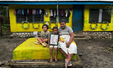 Fa'aoso Tuivale, 30, holds a picture of her three children who died in the 2019 measles epidemic in Samoa while sitting on their grave
