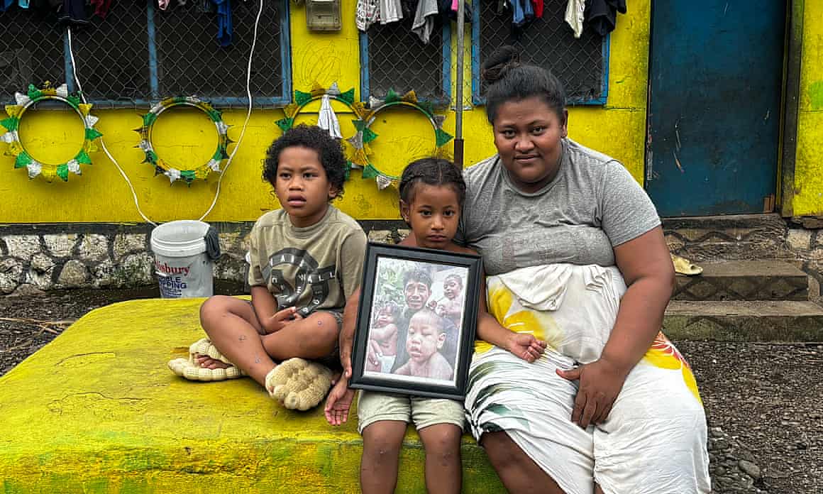 A woman and two children sit on top of a yellow-painted slab of stone, holding a photograph of three children