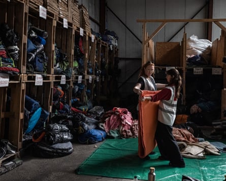 Two people fold a blanket in front of large shelves stacked with items