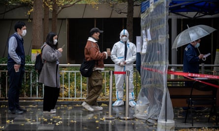 An epidemic control worker wears protective clothing as people queue at a Covid testing booth in Beijing.