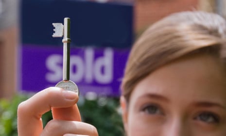 A young woman holding a door key in front of a sold sign