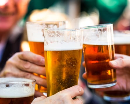 Close-up colour image depicting a group of people celebrating with a toast. The people cheer their glasses of beer (pints of beer) together in a gesture of celebration, togetherness and happiness. The people are defocused in the background, while focus is on the glasses of beer in the foreground.