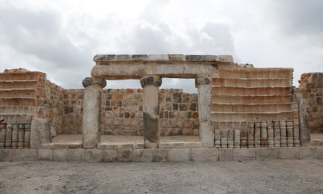 A white stone structure has walls on three sides and columns across the front with jars set into a section of the wall.