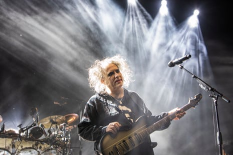 The Cure’s Robert Smith with guitar, light streaming down behind him, on stage in Leeds.