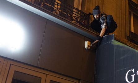 Un homme portant un bonnet s'accroche à un balcon pour couper l'alimentation d'une enseigne