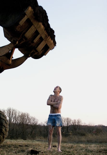 Steve-O, shirtless, looks up in fear at a digger bucket full of (possibly) manure over his head