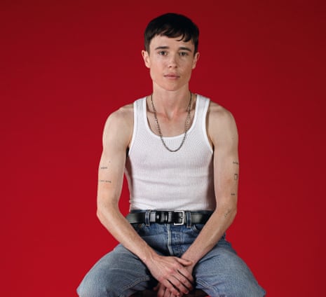 Elliott Page wearing jeans, a vest and a chain, against a red background