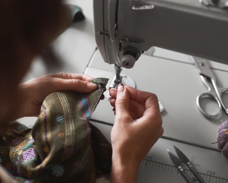 Closeup of hands pinning plaid fabric beside a sewing machine, with scissors nearby.