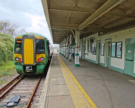 A train pulling into a platform with a turquoise and cream station building.
