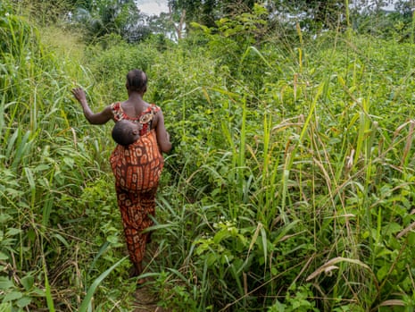 Marilou walks in a field of tall grass, carrying a grandchildren behind her in a harness.