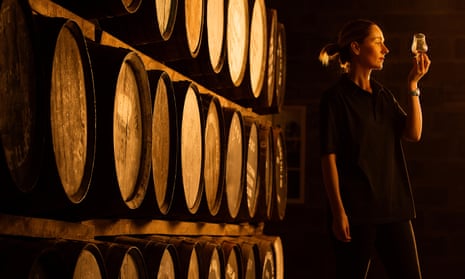 A female taster in a distillery checks a sample of whisky in a glass.