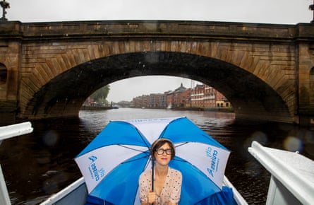 Emma in a boat on the river, holding an umbrella.