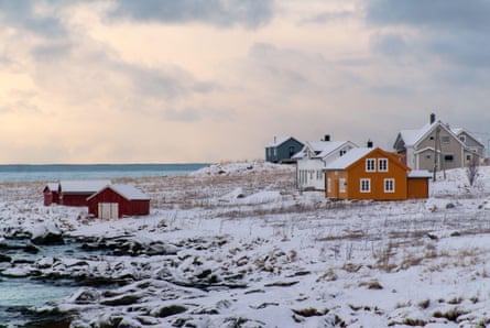 Colourful wooden buildings in a snowy landscape by the sea, against a cloudy sky