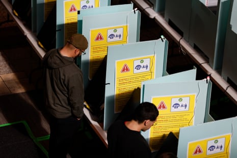 Voters stand at booths with yellow instructional signs, casting their ballots